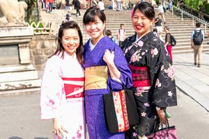 3 Frauen in verschiedenen Kimonos. Im hintergrund ist eine Treppe zu sehen.