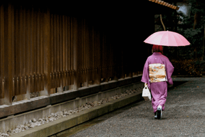 Kimono Nähen - Frau im Pinken Kimono und Schirm läuft an einer Wand entlang, sie trägt eine Handtasche.