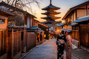 Frauen im Kimono auf japanischer Straße. In der Bildmitte im hintergrund ist ein Japanischer Schrein zu sehen.