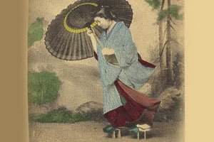 Altes Foto auf dem jemand mit einem Kimono, Geta und Regenschirm zu sehen ist.