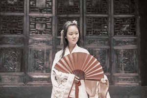 Frau vor einer verzierten Tür im Kimono. Sie trägt einen Sensu Handfächer.