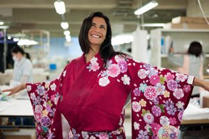 Eine Frau im rosa Kimono mit Blumen Motiven. Sie lächelt und schaut nach oben.